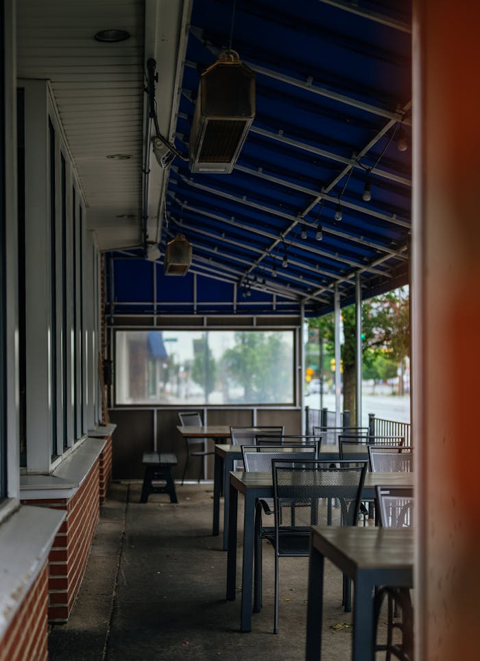 Quiet outdoor dining area with tables and chairs under a blue awning, ready for guests.